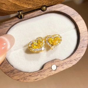 Macro shot of gold-plated heart stud earrings with yellow gemstones on a wooden jewelry box