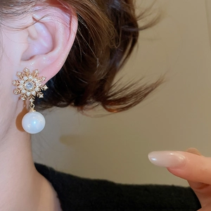 Close-up of snowflake pearl earring with gold zircon accents on female model ear
