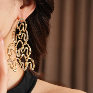 Close-up of gold irregular geometric wave earrings with pavé crystals on a model