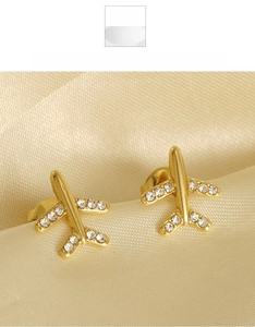 Détail de boucles d'oreilles avion dorées avec ailes en cristal sur fond satiné