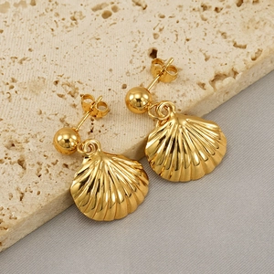 Golden shell earrings in stainless steel on a textured stone background for women