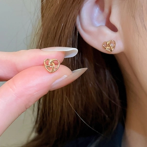 Close-up of gold hollow heart stud earrings showing detailed intertwined line design