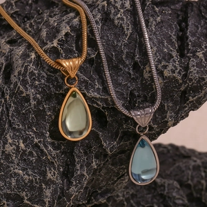 Macro detail of teardrop gemstone pendant on a gold snake chain over dark stone background