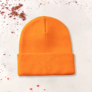 Detail of orange knitted beanie with pumpkin embroidery for Halloween on festive background
