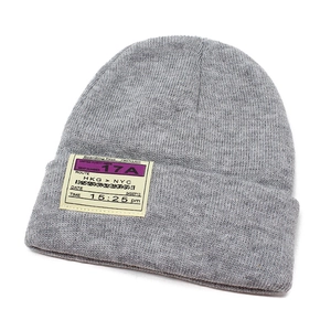 Detailed view of grey knitted beanie featuring a vintage yellow boarding pass patch
