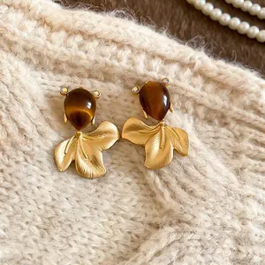 Golden fish earrings with brown catseye stone on cozy white knit sweater background