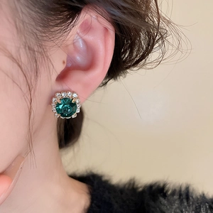 Vue rapprochée des boucles d'oreilles émeraude avec halo de cristal et finition dorée