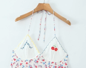 Detail view of floral embroidery and cherry motif on a white halter mini dress