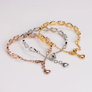 Three heart-shaped open bracelets in rose gold, silver, and gold stacked on a grey background