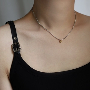 Close-up of minimalist gold heart pendant on a silver beaded chain worn on the neck