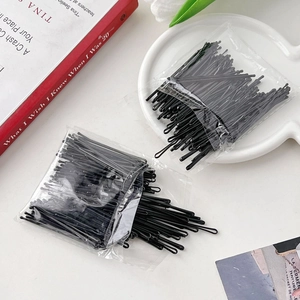 Close-up of black metal bobby pins in transparent plastic bags on a white desk setup