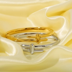 Polished gold and silver knotted bangles displayed on elegant yellow silk fabric background
