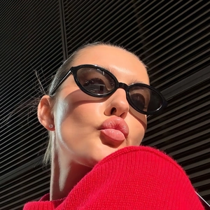 Fashionable black oval sunglasses on model in red knit sweater with stylish lighting