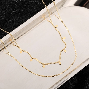 Close-up of double-layered gold titanium necklace with rhombus charms on a silver tray