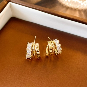 Macro shot of gold-plated C-shaped earrings with square-cut zircon and pyramid studs