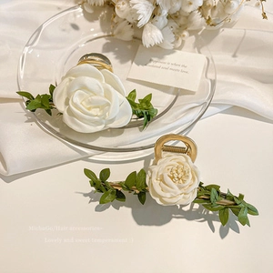 Detail of white rose hair claw clip with silk petals and green leaves on gold alloy