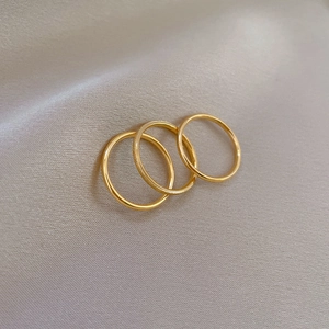 Detailed view of three minimalist gold titanium steel rings on soft silk fabric background
