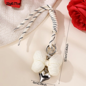 Detail of beige knitted bow keychain with silver heart charm and black and white cord