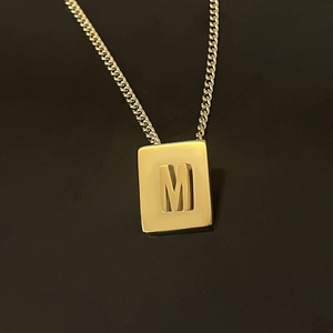 Macro shot of gold 18K plated stainless steel square pendant with embossed letter M detail