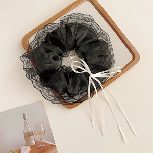 Detail of oversized black lace scrunchie with creamy white satin ribbon bow on wooden tray