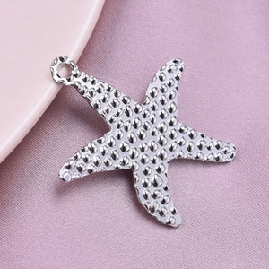 Detailed macro view of silver starfish pendant with textured finish on pink fabric