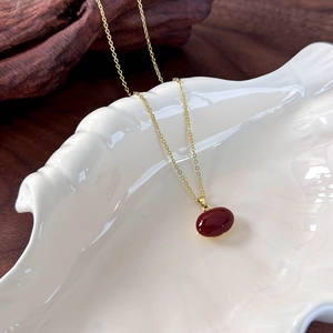 Detail view of a gold chain necklace with a red bean pendant in a shell tray
