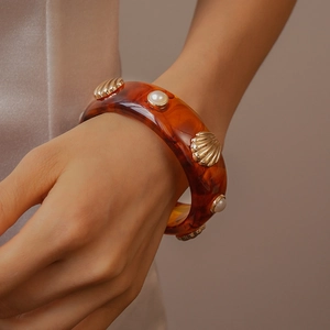 Gros plan d'un bracelet manchette en résine ambrée avec coquillages dorés et perles