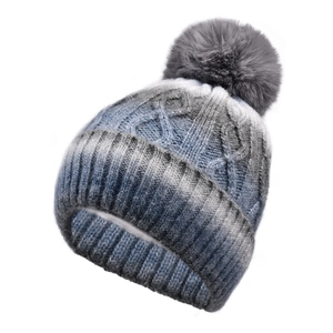 Detail of cable knit pattern and grey faux fur pompom on ombré winter beanie hat