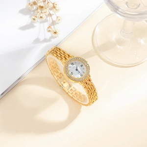 Detailed close-up of a gold quartz watch with a diamond-inlaid bezel on a beige setting