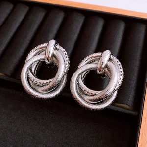 Macro shot of silver knot earrings with matte and polished rings on velvet tray