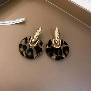Detail of gold hammered metal and round leopard print acrylic earrings on a tray