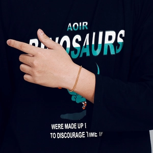 Close-up of a gold-plated pearl chain bracelet on a male wrist over a dark shirt