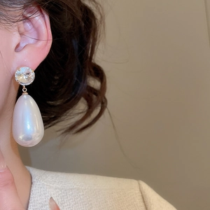 Close-up of a teardrop pearl earring with round crystal stud on a model's ear
