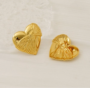 Detail of gold heart earrings showing textured wrinkles and needle clasp on beige surface