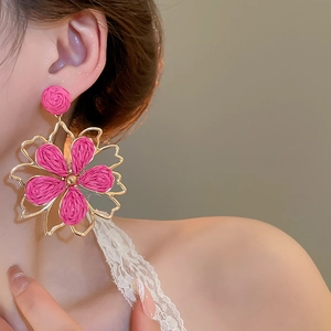 Detail von rosa Raffia gewebten Blumenohrringen mit goldenem Metallrahmen am Model