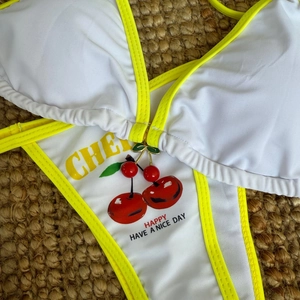 Close-up of cherry print bikini with yellow trim and decorative cherry charms on straw mat