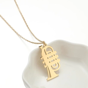 Polished golden trumpet musical instrument pendant necklace on white ceramic tray