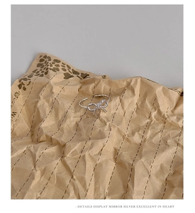 Detail view of silver bow-shaped hollow twist ring on textured paper background