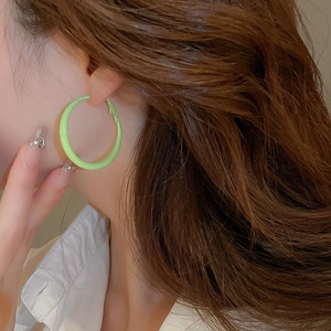 Close-up of a large fluorescent green hoop earring worn on an ear with minimalist style