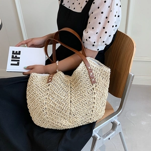 Close-up of beige woven straw tote bag with brown leather handles and X-stitch details