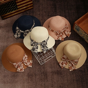 Detail of woven straw sun hats featuring elegant checkered ribbons and large bow decorations
