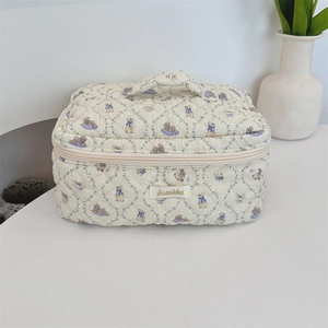 Close-up of beige quilted cotton cosmetic bag featuring rabbit patterns and top handle