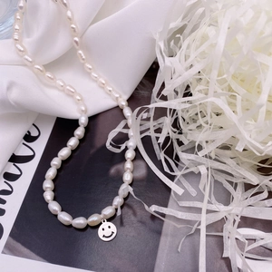 Detail of freshwater pearl necklace with silver smiley face pendant on white silk fabric