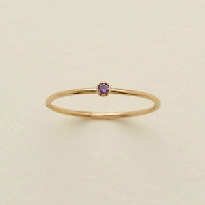 Detailed macro shot of a gold ring with a round purple gemstone on textured paper