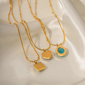 Detail of gold necklaces with square, heart and blue cat-eye stone charms on white silk