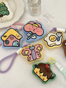 Plush cartoon bag pendants with colorful embroidery and woven cords on a white tray