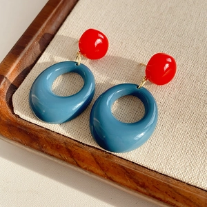 Detail of red and blue geometric resin earrings on a wooden tray with soft shadows