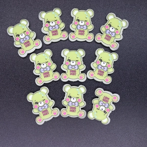Macro view of 10 light green resin bear charms with purple bows and HUG ME text