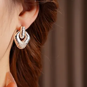 Golden geometric intertwined hoop earrings with textured finish and zircon accents on model
