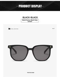 Detail of black sunglasses with square frames and golden rivet accents on a gray background